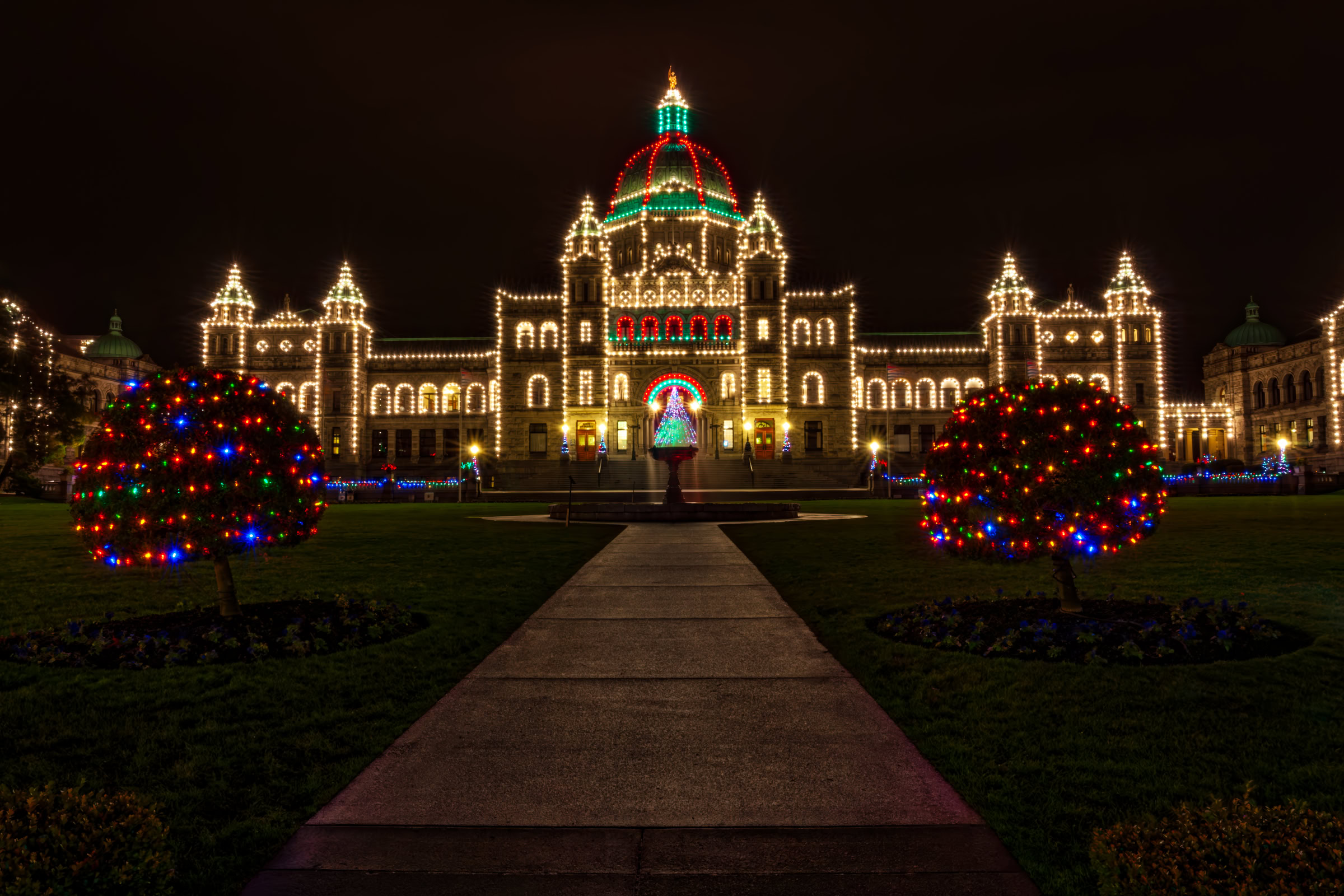 BC Parliament Christmas lights print showing the Parliament Buildings outlined in bulbs with a red and green dome on a rainy night in Victoria, BC, by James Wheeler.