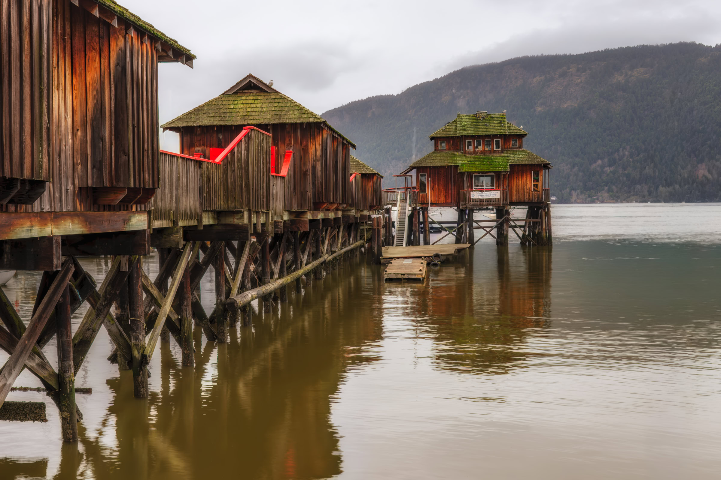 Cowichan Bay wall art showing the Maritime Centre's weathered wood pavilions on their pier over still water, Vancouver Island, BC, by James Wheeler.
