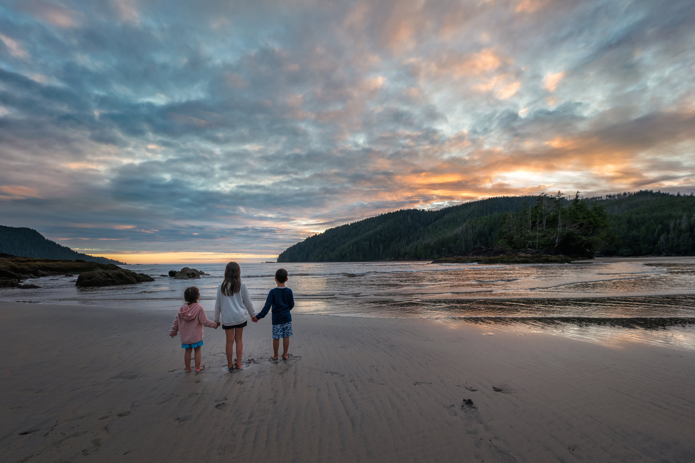 Cape Scott Provincial Park at sunset, three kids holding hands on the sand at San Josef Bay, Vancouver Island, BC, by James Wheeler.