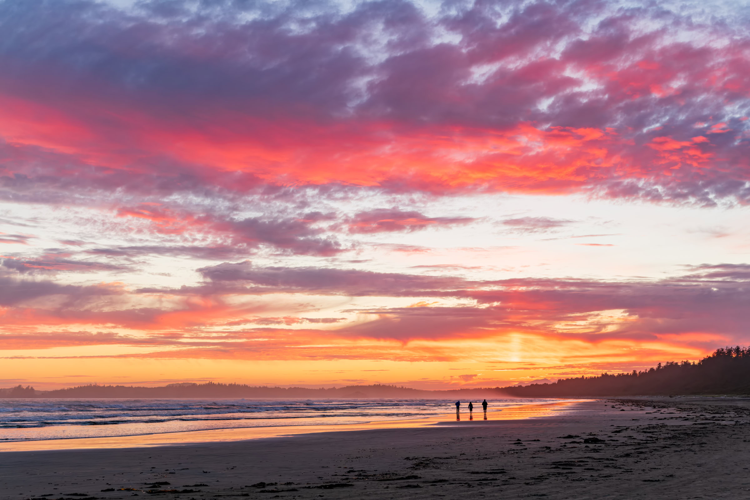 Long Beach Tofino wall art of three people walking the tideline under pink sunset clouds, Pacific Rim National Park, BC, by James Wheeler.