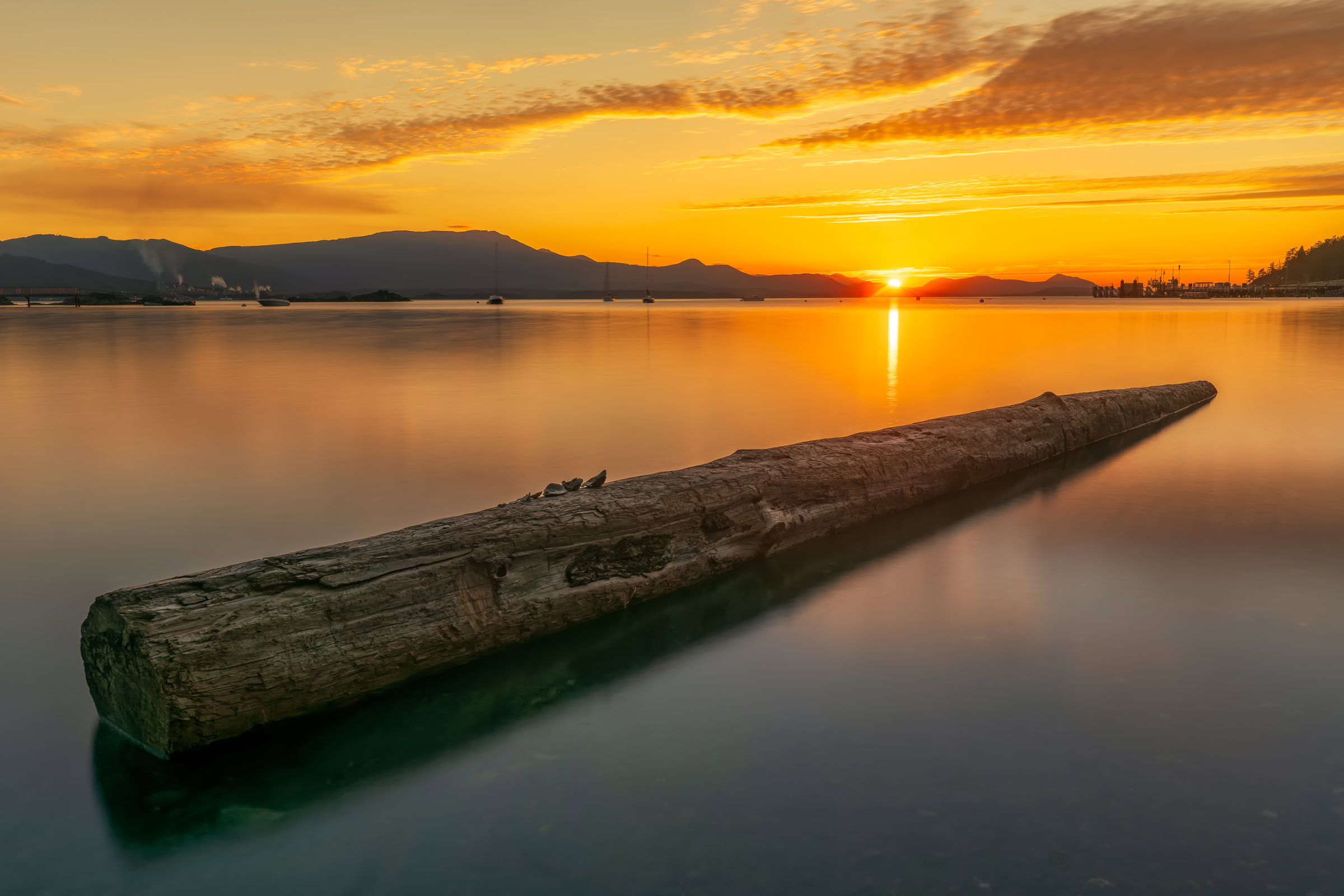 Salt Spring Island sunset photo print of a drift log in calm water at Vesuvius Bay, the sun setting behind Vancouver Island, BC, by James Wheeler.