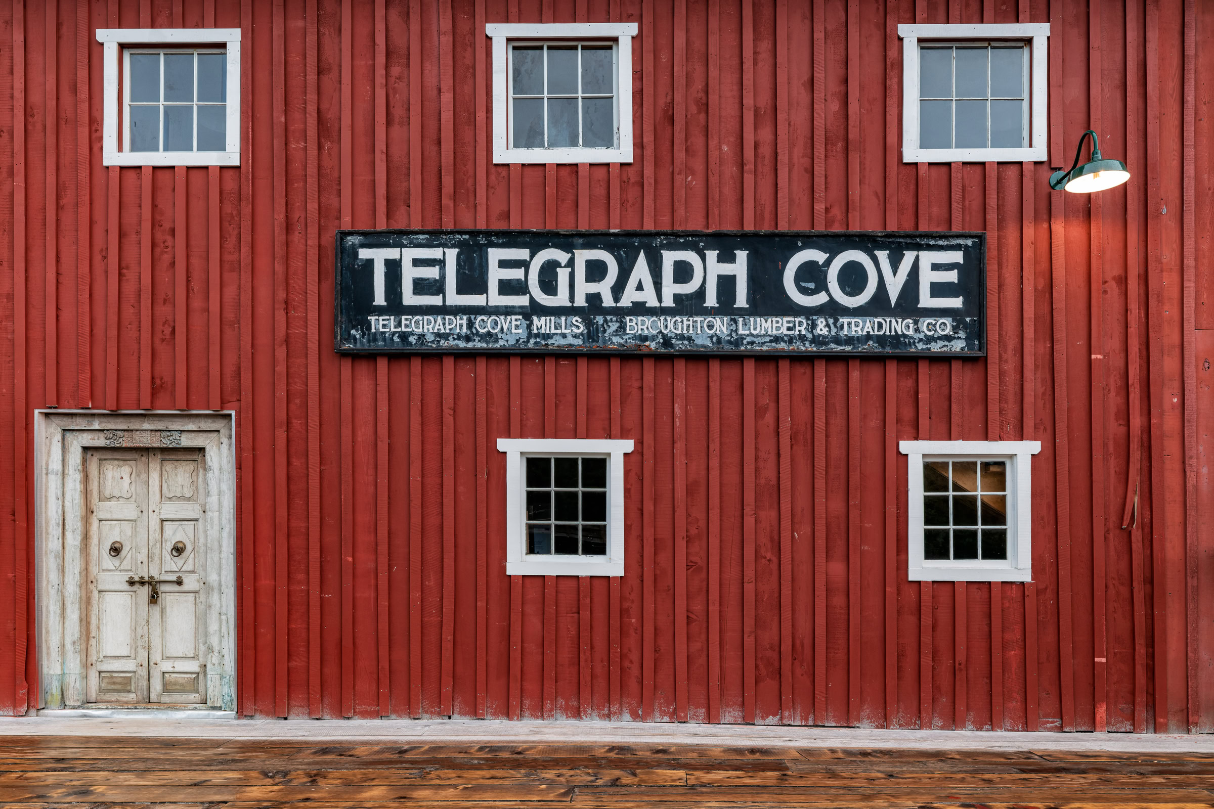 Telegraph Cove wall art showing the red boardwalk building that housed the whale museum, with its Telegraph Cove Mills sign, on northern Vancouver Island, BC, by James Wheeler.
